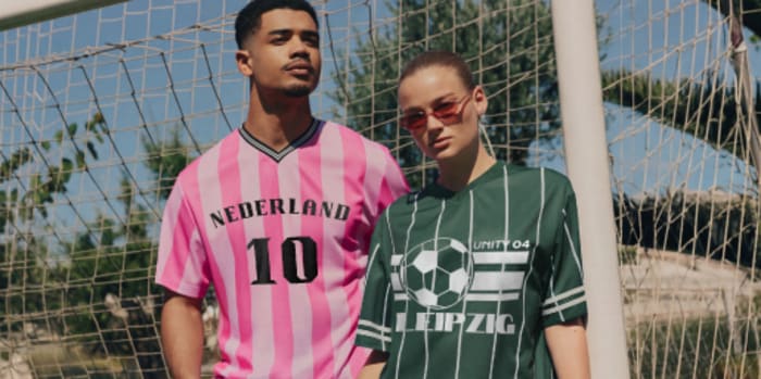 Two people stand in front of a football goal wearing printed football jerseys with custom designs and club motifs.