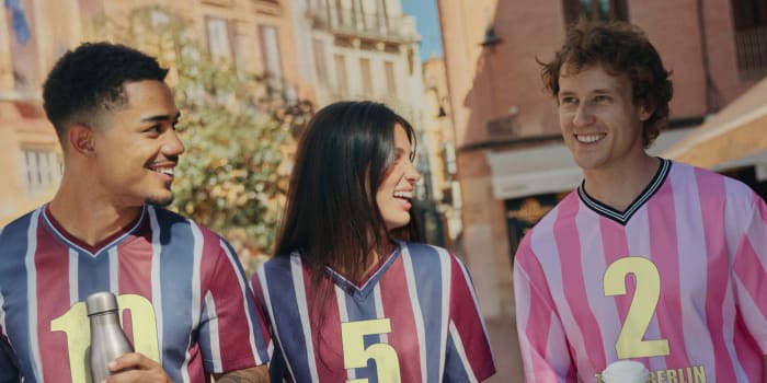 Three people walk through a city smiling in striped football jerseys with personalised numbers and team names.