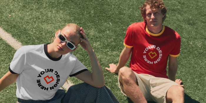 Two people sit on a football pitch wearing custom retro shirts with the text “Your design here”.