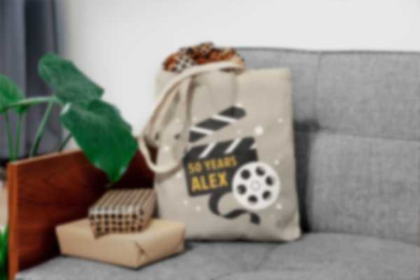 Tote bag personnalisé pour les 50 ans posé sur un canapé entouré d’autres cadeaux d’anniversaire 