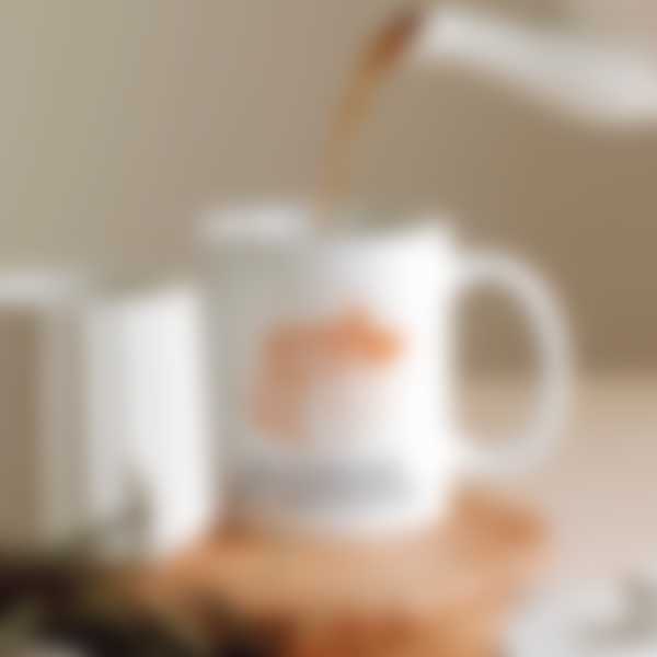 A teapot pours tea into a white mug with a photo print